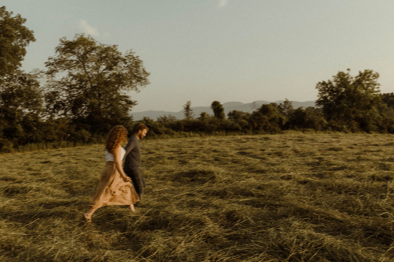 Couple running through open field in Upstate New York with golden hour light.