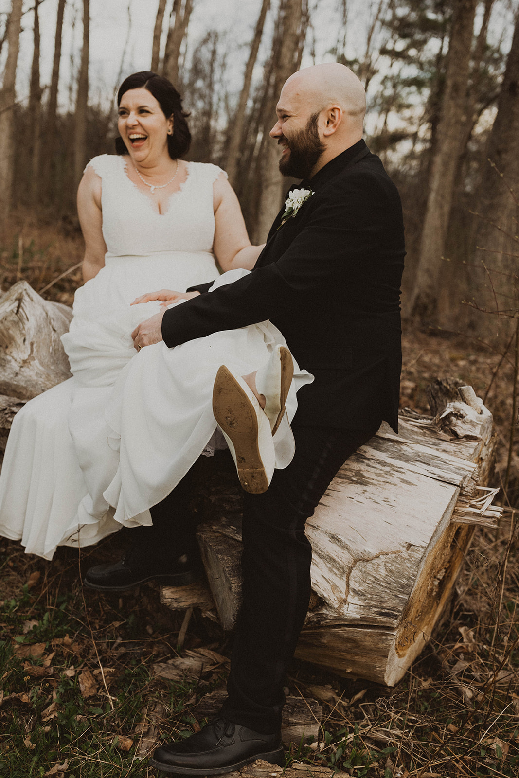 Bride and groom sit on a log on their dreamy upstate New York wedding day