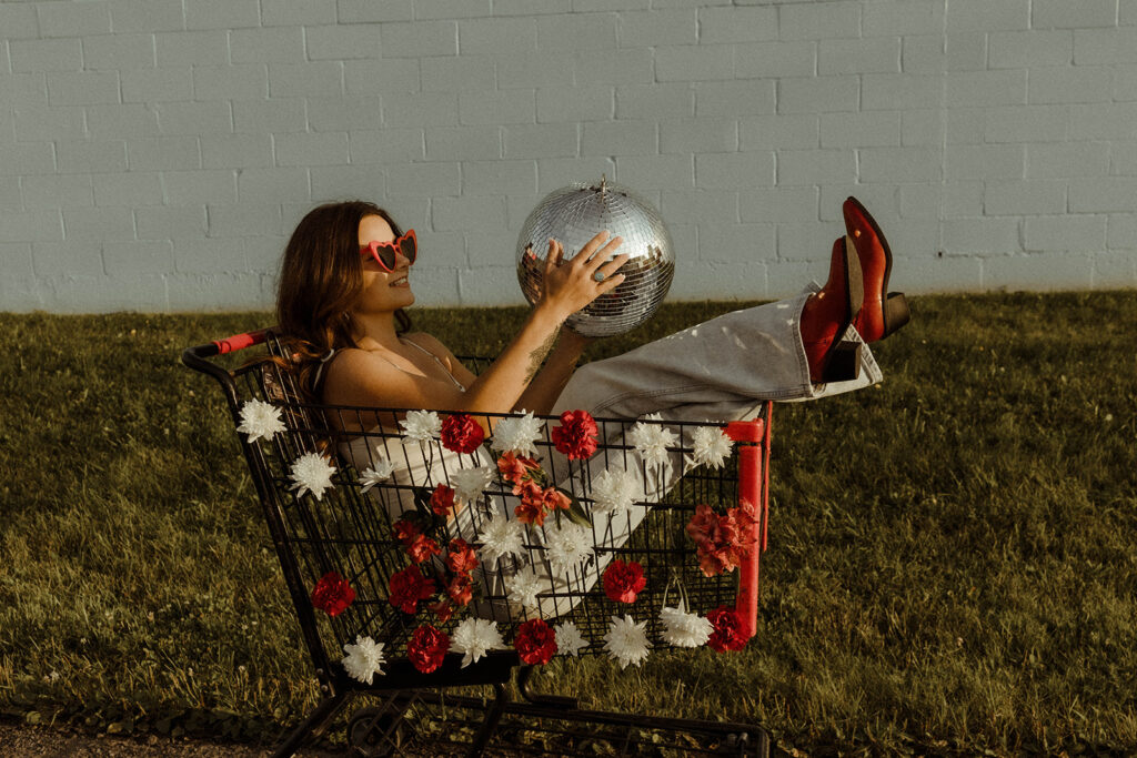 photo of stylish woman with heart shaped glasses in floral shopping cart holding a disco ball.