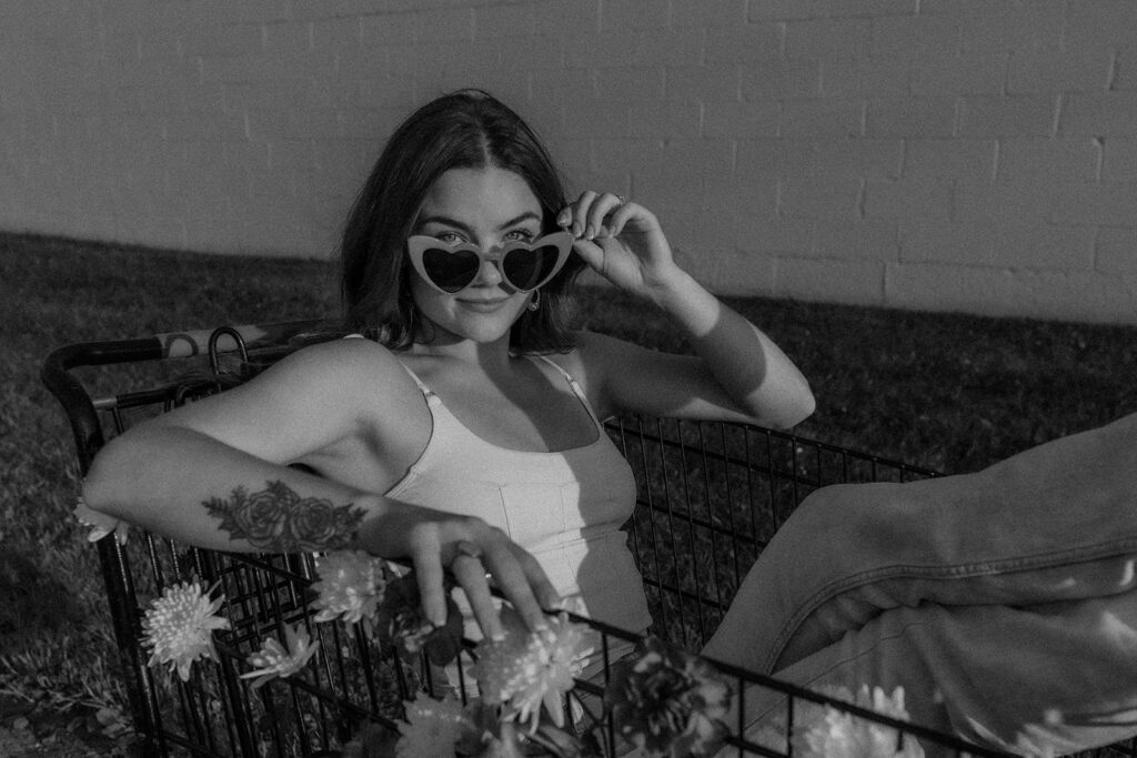 black and white photo of stylish woman with heart shaped glasses in floral shopping cart. 
