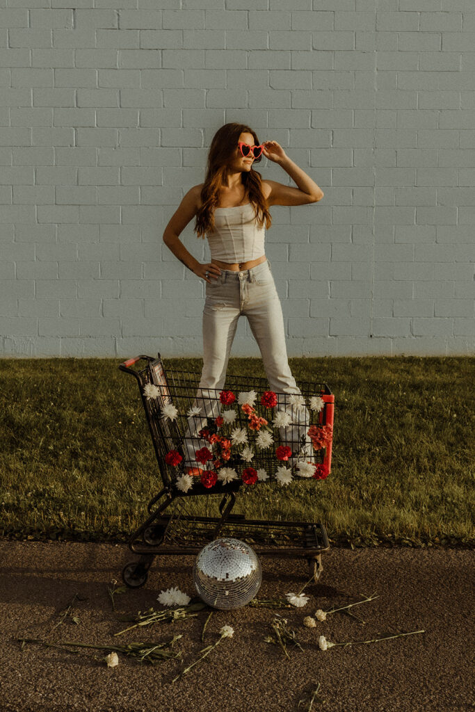 photo of stylish woman with heart shaped glasses in floral shopping cart holding a disco ball.
