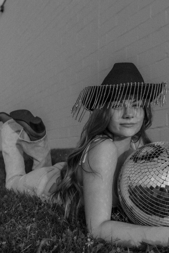 photo of stylish woman with  a cowgirl hat on and holding a disco ball.