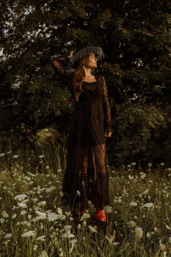 western woman with cowgirl hat and black dress standing in wildflower field.