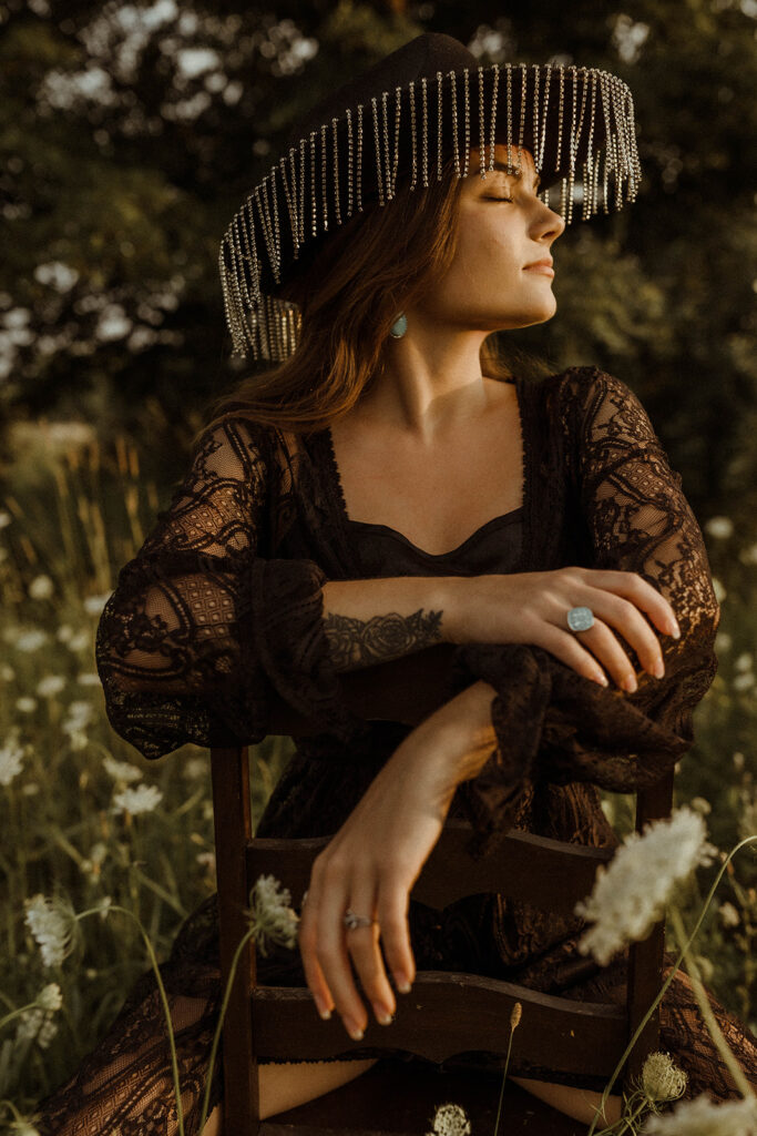 western woman with black dress and cowgirl hat on sitting in wildflower field.