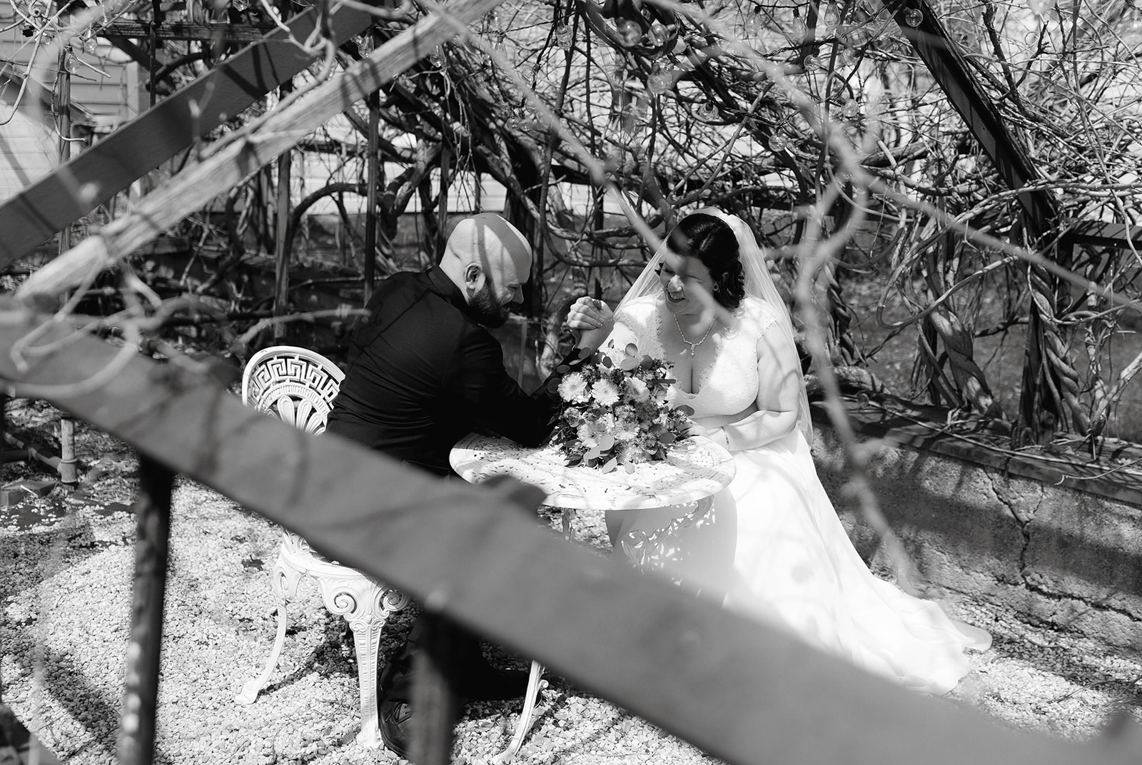 Bride and groom arm wrestle on a small picnic table chatting about their wedding day