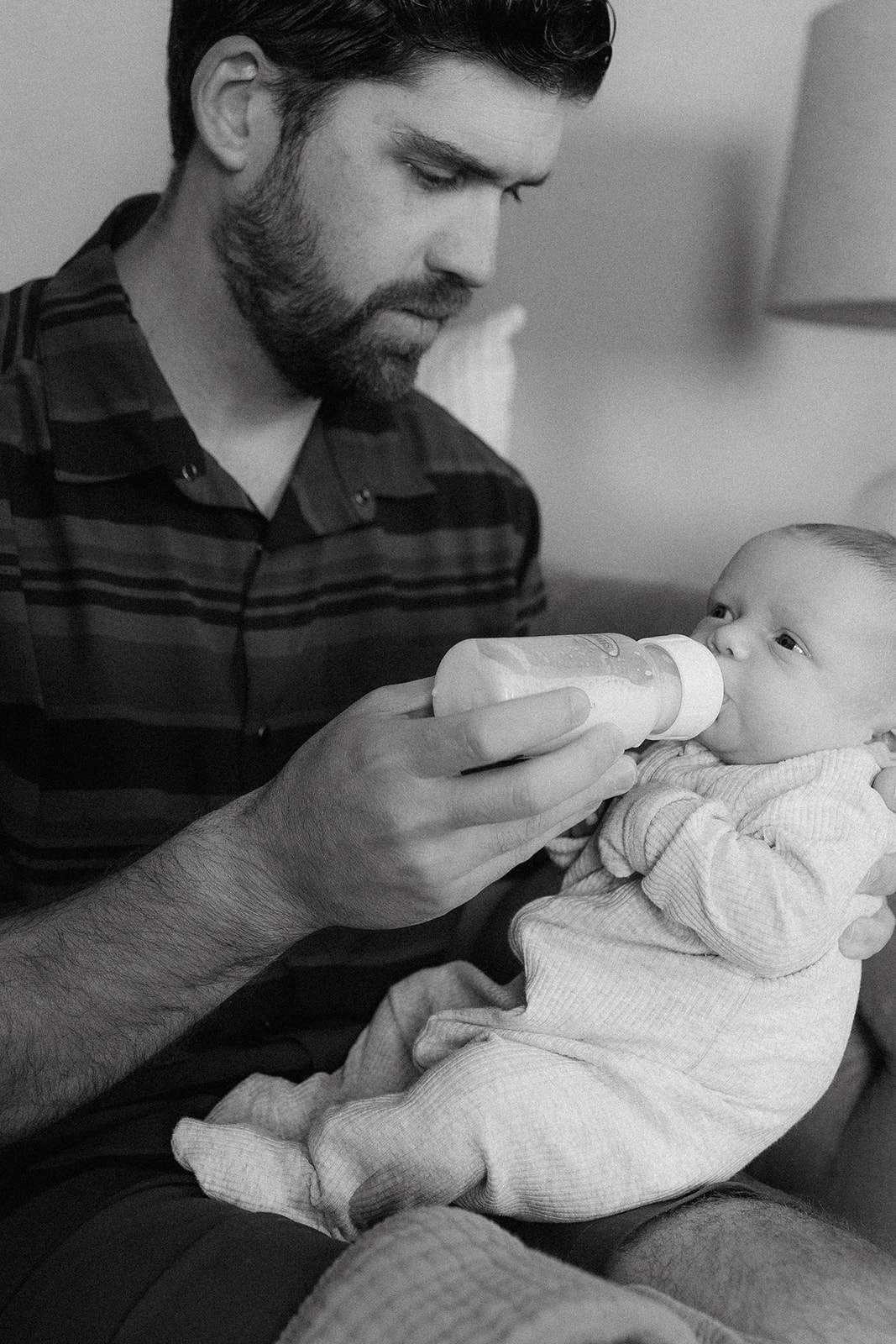 A beautiful new dad feeds his new son during their in home newborn photography session